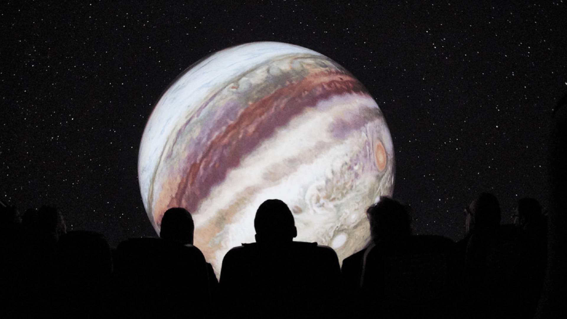 Audiences watching a projected film on a domed screen.