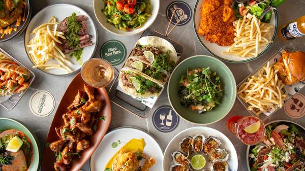 A dining table covered in pub food served on plates of different colours and sizes. There are tacos, chicken schnitzel and oysters.