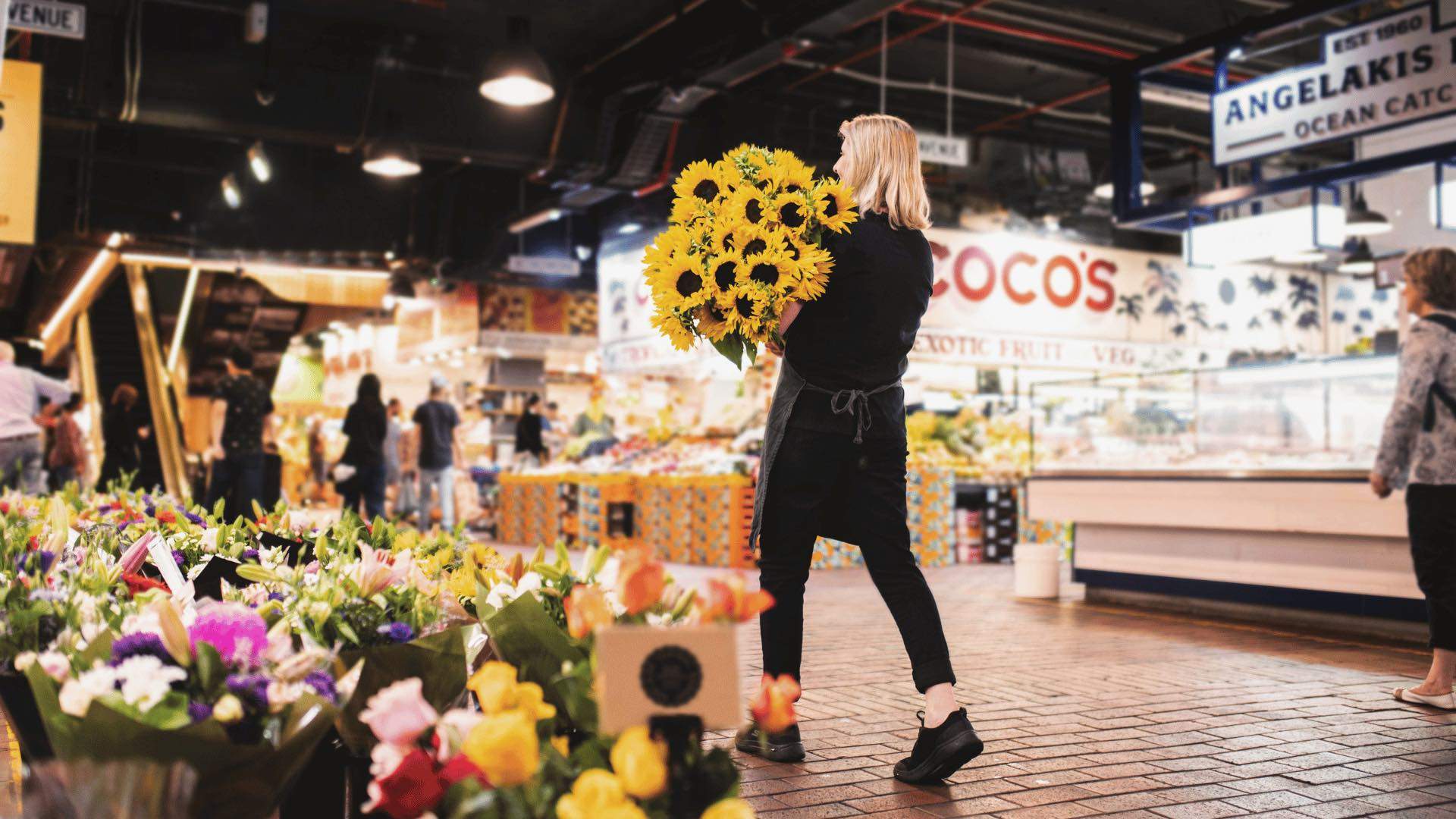 A woman carrying a bouquet of sunflowers in the Adelaide Central Market.