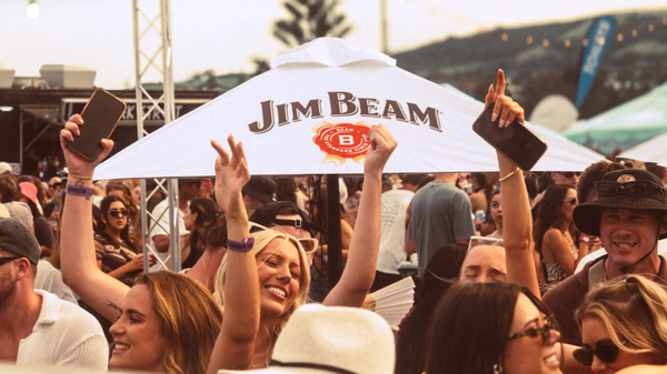 A crowd dances in front of a Jim Beam branded umbrella at a festival