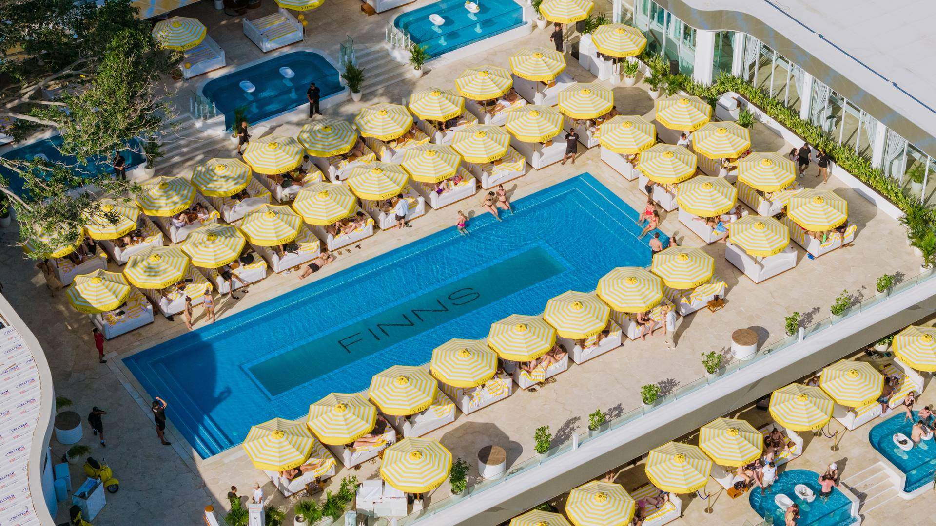 Aerial view of FINNS Beach Club's pool deck in Canggu, Bali, lined with yellow and white striped umbrellas