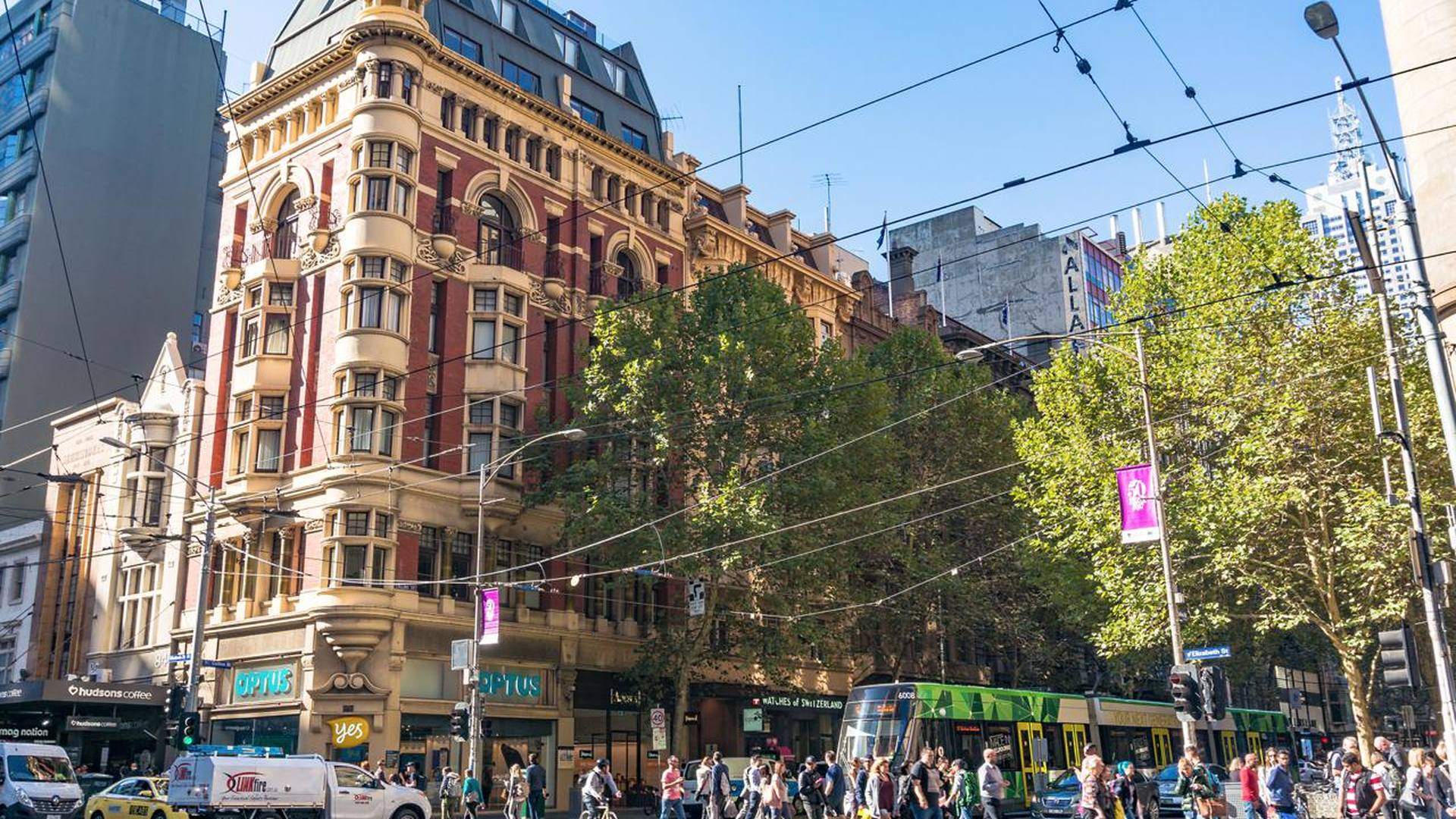 Pedestrians and a tram crossing a busy Collins Street intersection in Melbourne
