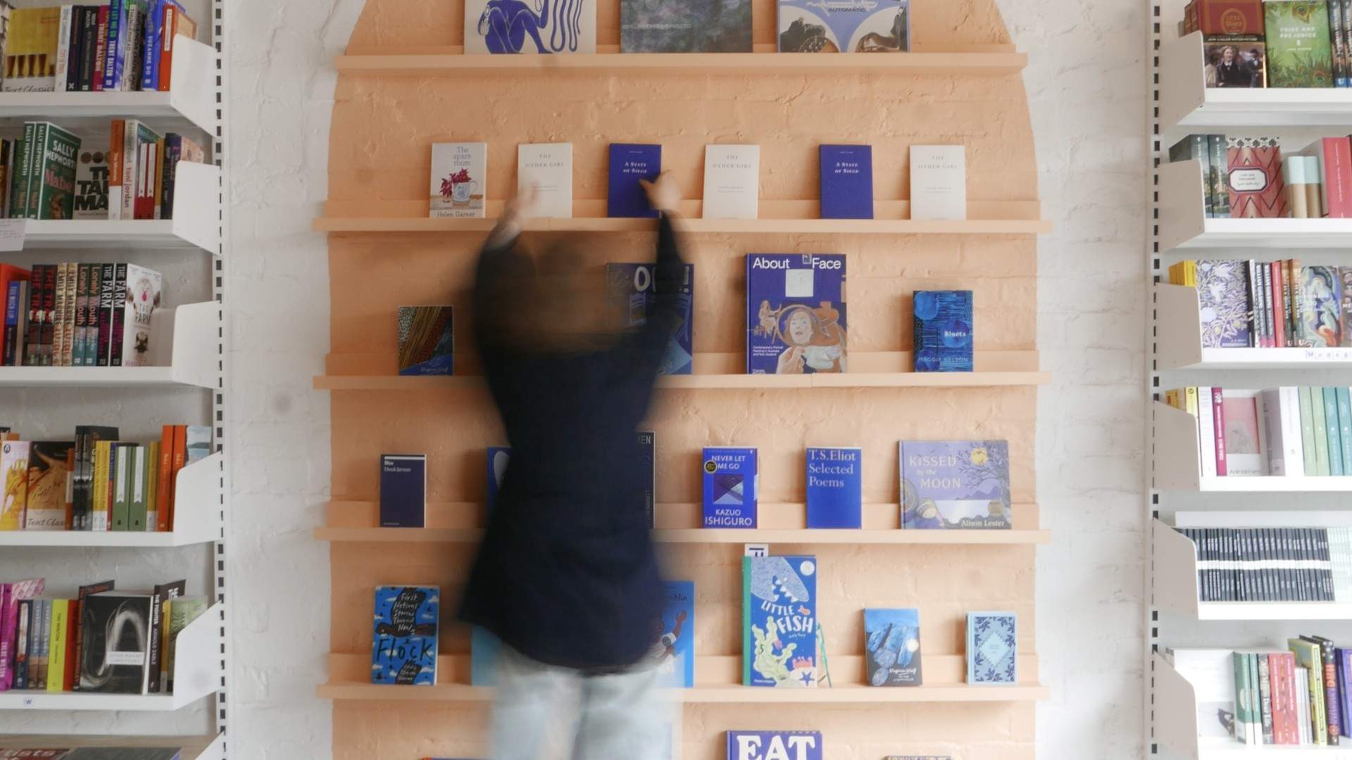 A staff member arranging books on Fino Books' arched peach display shelf