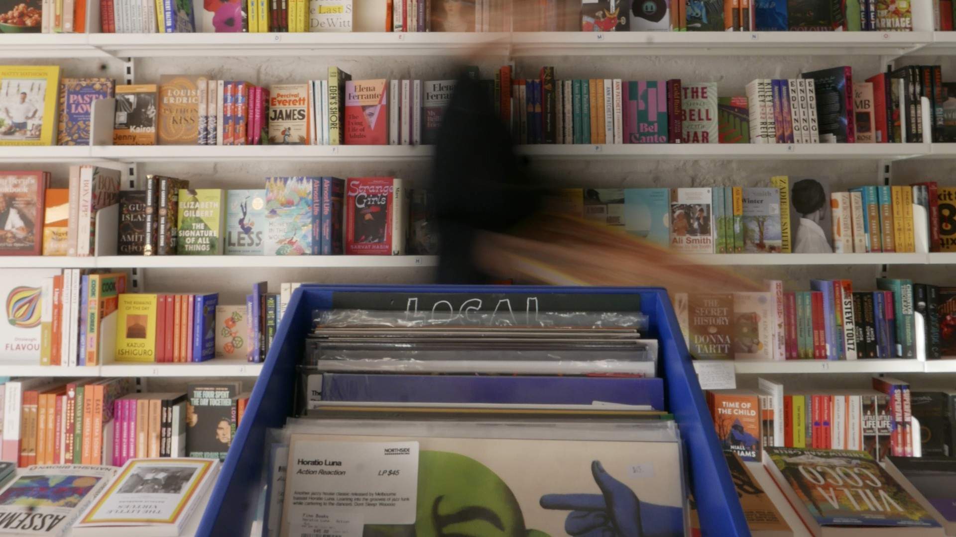 A blue crate of Northside Records vinyl in front of colourful bookshelves at Fino Books