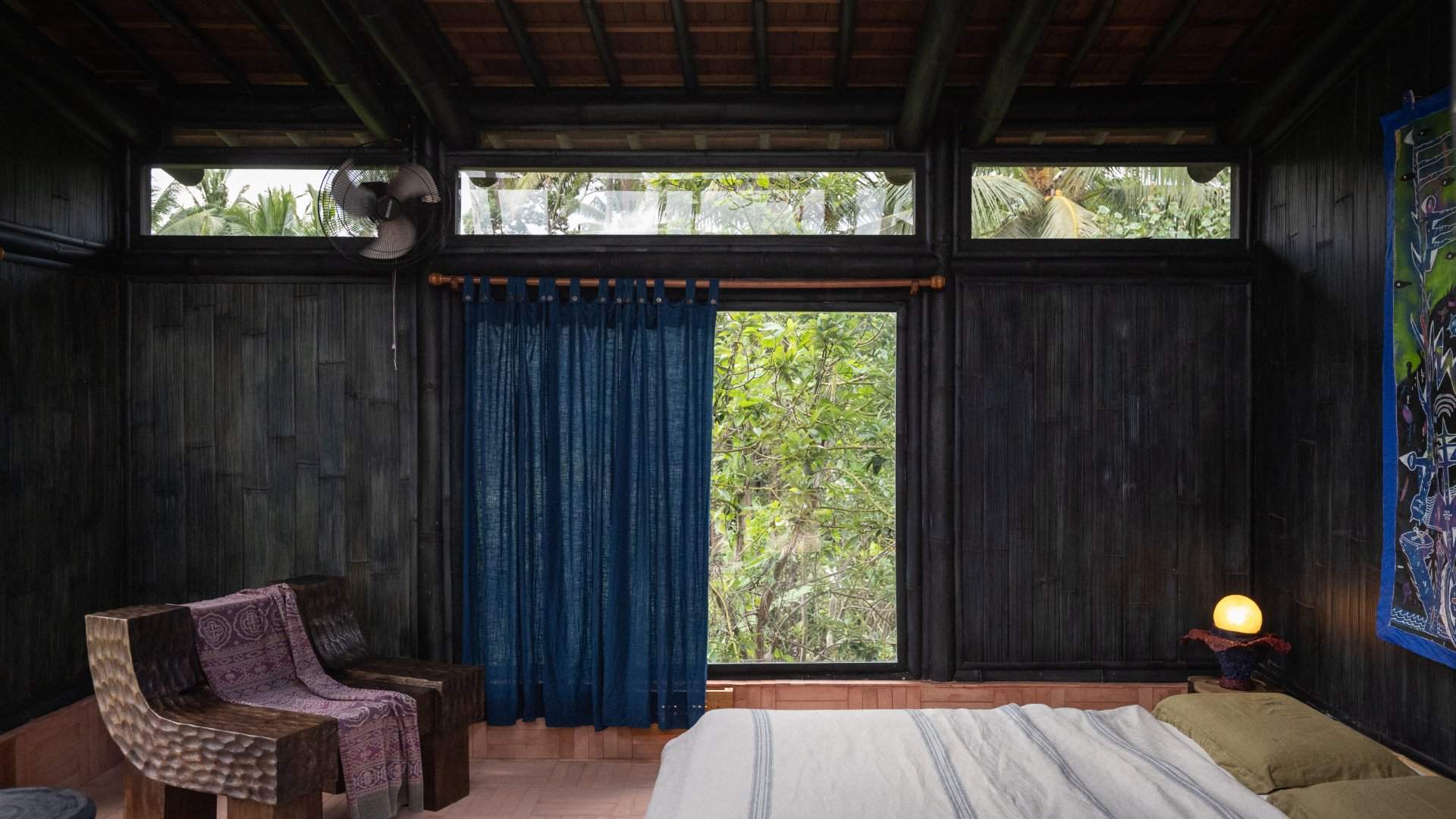 Dark timber-lined Sundust suite at Moon Gang Ubud with a blue curtain opening onto greenery